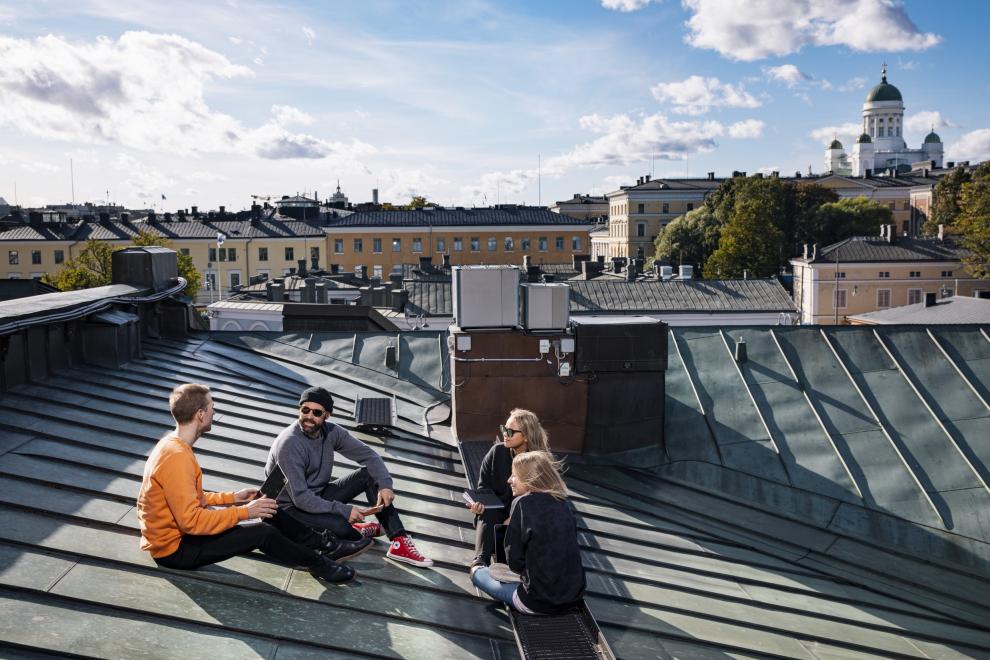 Neljä henkilöä istuu talon katolla Helsingin keskustassa