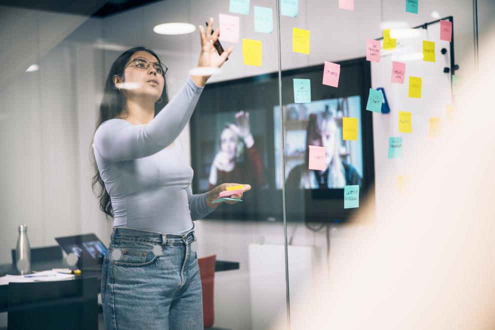 Nainen liimaa post-it -viestilappuja kokoushuoneen lasiseinään