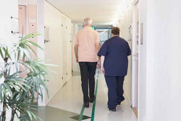Helsingin kaupungin aineistopankki / Kaisa Sunimento Sairaanhoitaja ja iäkäs mies kävelevät sairaalan käytävällä. Kuvaaja: Kaisa Sunimento.