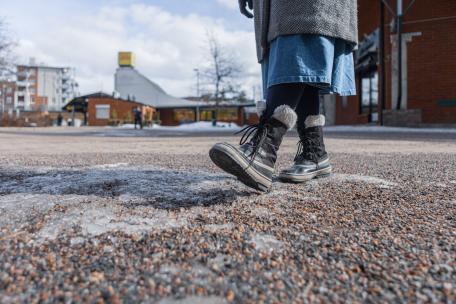 Nainen kävelee hiekkatiellä kaupungissa.